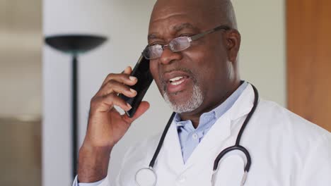 Afroamerikanischer-Leitender-Männlicher-Arzt-Im-Weißen-Kittel,-Der-Auf-Dem-Smartphone-Spricht