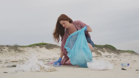 Kaukasische-Frau-Mit-Latexhandschuhen,-Die-Müll-Vom-Strand-Sammelt-Und-Nach-Vorne-Blickt
