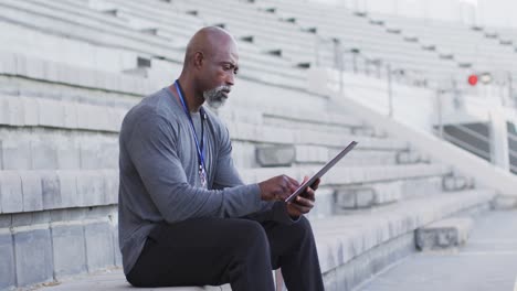 African-american-male-coach-sitting,-time-checking-and-making-notes