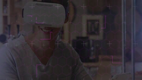 Hexagonal-shapes-and-data-processing-against-caucasian-man-wearing-vr-headset-using-digital-tablet