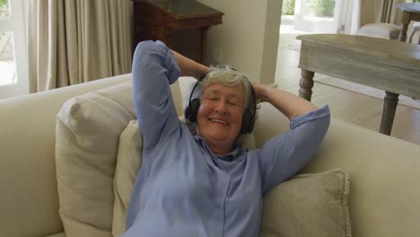 Caucasian-senior-woman-wearing-headphones-smiling-while-listening-to-music-at-home