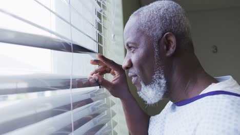 Afroamerikanischer-Männlicher-Patient,-Der-Lächelnd-Auf-Das-Fenster-Im-Krankenhauszimmer-Blickt
