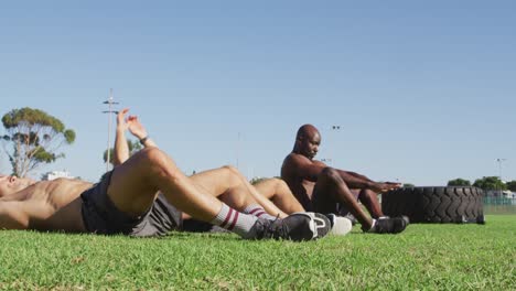 Diverse-group-of-three-fit-men-exercising-outdoors,-doing-sit-ups
