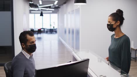 Mixed-race-woman-in-face-mask-has-temperature-checked-by-male-colleague-at-office-reception-desk