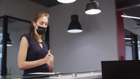 Caucasian-woman-in-face-mask-disinfects-hands-and-signs-in-at-office-reception-desk
