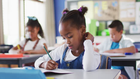 Portrait-of-african-american-schoolgirl-sitting-in-classroom,-making-notes