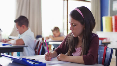 Portrait-of-caucasian-schoolgirl-sitting-in-classroom,-making-notes