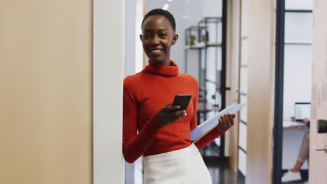 Porträt-Einer-Afroamerikanischen-Frau,-Die-Lächelt,-Während-Sie-Im-Büro-Ihr-Smartphone-Benutzt