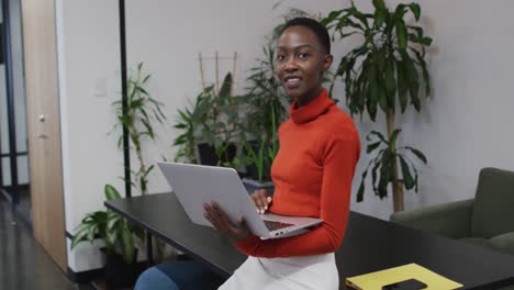 Porträt-Einer-Afroamerikanischen-Frau,-Die-Lächelt,-Während-Sie-Im-Büro-Einen-Laptop-Benutzt