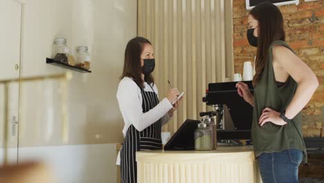 Caucasian-waitress-wearing-face-mask-taking-order-from-caucasian-female-customer