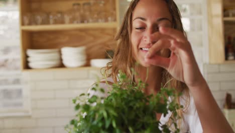 Smiling-caucasian-woman-touching-plant-in-cottage-kitchen