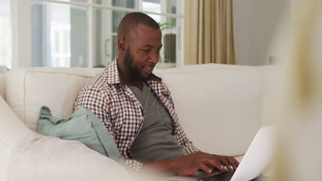 African-american-man-using-laptop-while-sitting-on-the-couch-at-home