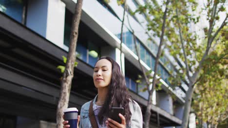 Mujer-Asiática-Caminando-Usando-Un-Teléfono-Inteligente-Y-Bebiendo-Café-Para-Llevar