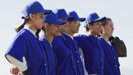 Happy-diverse-team-of-female-baseball-players-standing-in-line-with-arms-around-each-other-singing