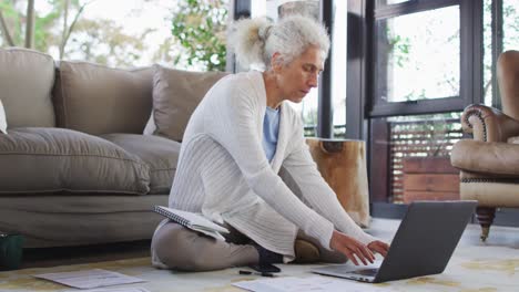 Senior-mixed-race-woman-sitting-on-floor-using-laptop