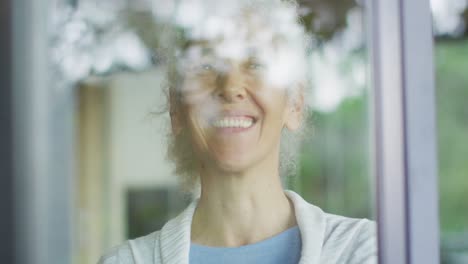 Senior-mixed-race-woman-looking-through-window-and-smiling
