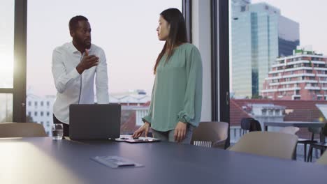 Video-of-two-diverse-male-and-female-colleagues-discussing-and-using-laptop-standing-in-office