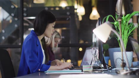 Video-Einer-Asiatischen-Geschäftsfrau,-Die-Nachts-Im-Büro-Mit-Einer-Kollegin-An-Einem-Laptop-Arbeitet
