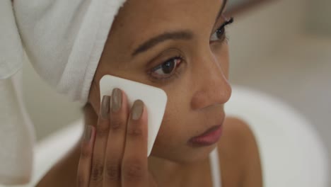 Mixed-race-woman-wearing-towel-on-head-cleaning-her-face