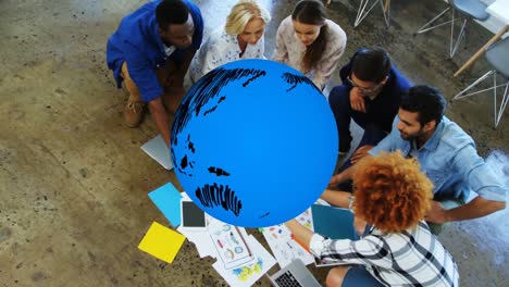 Animation-of-blue-globe-rotating-over-diverse-creative-colleagues-brainstorming-on-office-floor