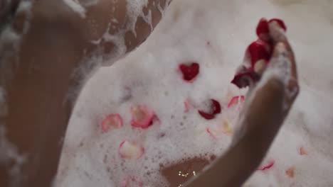 Hands-of-african-american-attractive-woman-taking-bath-with-foam-and-rose-petals