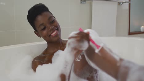 Smiling-african-american-attractive-woman-shaving-legs-in-foam-bath-in-bathroom