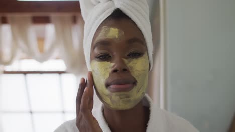 Portrait-of-african-american-attractive-woman-applying-face-mask-in-bathroom