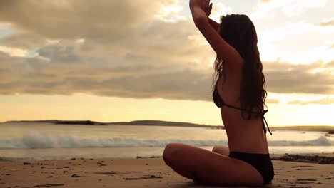 Peaceful-brunette-meditating-on-the-sand-at-sunset