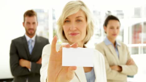 Smiling-businesswoman-showing-her-card-with-team-behind-her