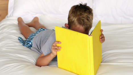 Little-boy-reading-yellow-book-on-bed