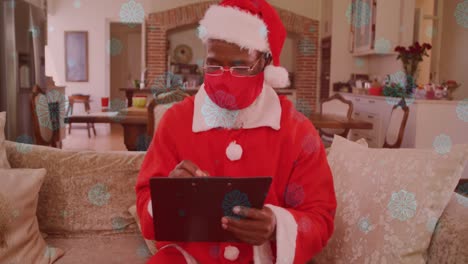 Animation-of-snow-falling-over-man-wearing-santa-claus-costume-and-face-mask-with-clipboard