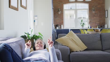 Relaxed-senior-caucasian-woman-in-living-room-lying-on-sofa,-wearing-headphones