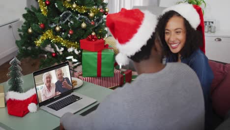 Glückliches-Afroamerikanisches-Paar-Bei-Einem-Videoanruf-Auf-Einem-Laptop-Mit-Einem-älteren-Paar-Zur-Weihnachtszeit