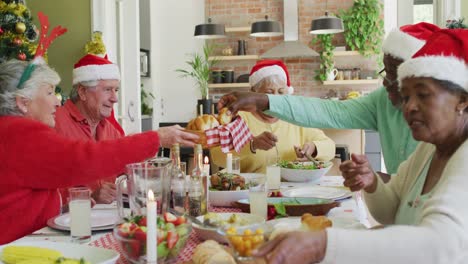 Group-of-happy-diverse-senior-friends-in-santa-hats-making-a-toast-at-christmas-dinner-table-at-home