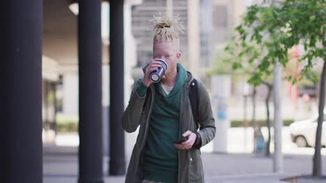 Thoughtful-albino-african-american-man-with-dreadlocks-drinking-coffee-and-using-smartphone
