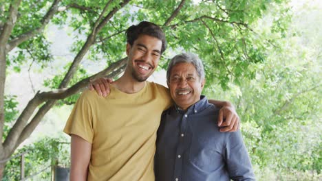 Cheerful-biracial-father-and-son-standing-with-arms-around-shoulders-smiling-to-camera