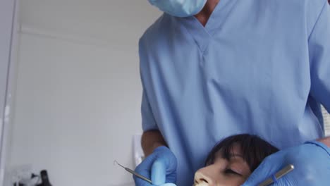 Kaukasischer-Männlicher-Zahnarzt-Mit-Gesichtsmaske-Untersucht-Die-Zähne-Einer-Patientin-In-Einer-Modernen-Zahnklinik