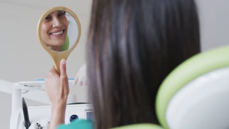 Biracial-Weibliche-Patientin,-Die-Zähne-Betrachtet-Und-Im-Spiegel-In-Einer-Modernen-Zahnklinik-Lächelt