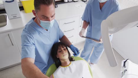 Kaukasischer-Männlicher-Zahnarzt-Mit-Gesichtsmaske-Untersucht-Die-Zähne-Einer-Patientin-In-Einer-Modernen-Zahnklinik