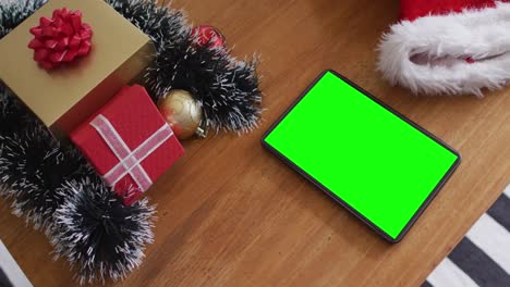 Tablet-with-green-screen-on-table-with-santa-hats-and-christmas-presents