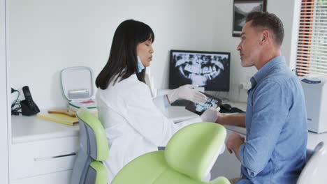 Biraziale-Zahnärztin-Mit-Gesichtsmaske-Untersucht-Die-Zähne-Eines-Männlichen-Patienten-In-Einer-Modernen-Zahnklinik