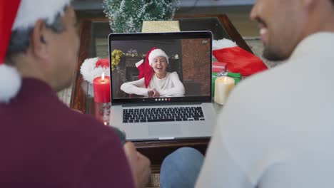 Smiling-biracial-father-and-son-using-laptop-for-christmas-video-call-with-woman-on-screen