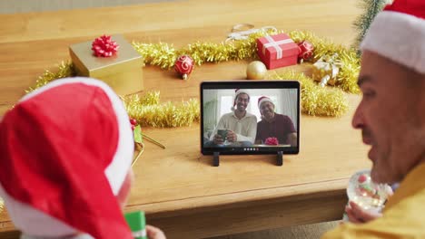 Kaukasischer-Vater-Und-Sohn-Mit-Weihnachtsmützen-Nutzen-Tablet-Für-Weihnachtsvideoanruf-Mit-Der-Familie-Auf-Dem-Bildschirm