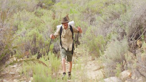Smiling-caucasian-male-survivalist-trekking-through-wilderness-with-backpack-and-walking-poles