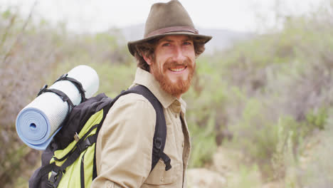 Portrait-of-smiling-bearded-caucasian-male-survivalist-trekking-through-wilderness-with-backpack