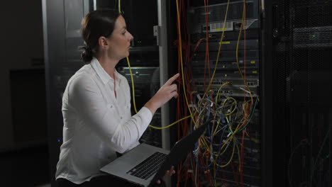 Caucasian-female-it-technician-using-laptop,-pointing-and-checking-computer-server