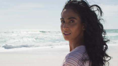 Portrait-of-happy-hispanic-woman-turning-around-on-beach-in-sun