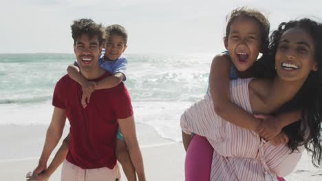 Happy-hispanic-parents-carrying-children-on-piggyback-on-beach