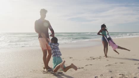 Happy-hispanic-parents-playing-with-children-on-beach-in-sun