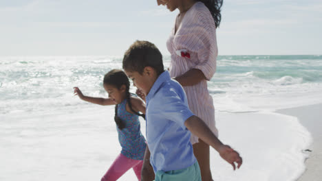 Midsection-of-happy-hispanic-moter-with-daughter-and-son-walking-on-beach